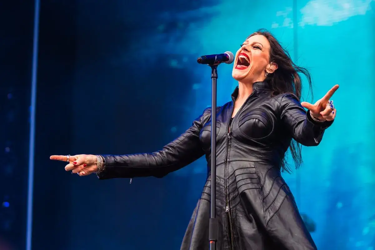 Floor Jansen sjunger passionerat på scen i en svart läderklänning, med mikrofonen nära munnen. Hon pratar svenska med publiken.