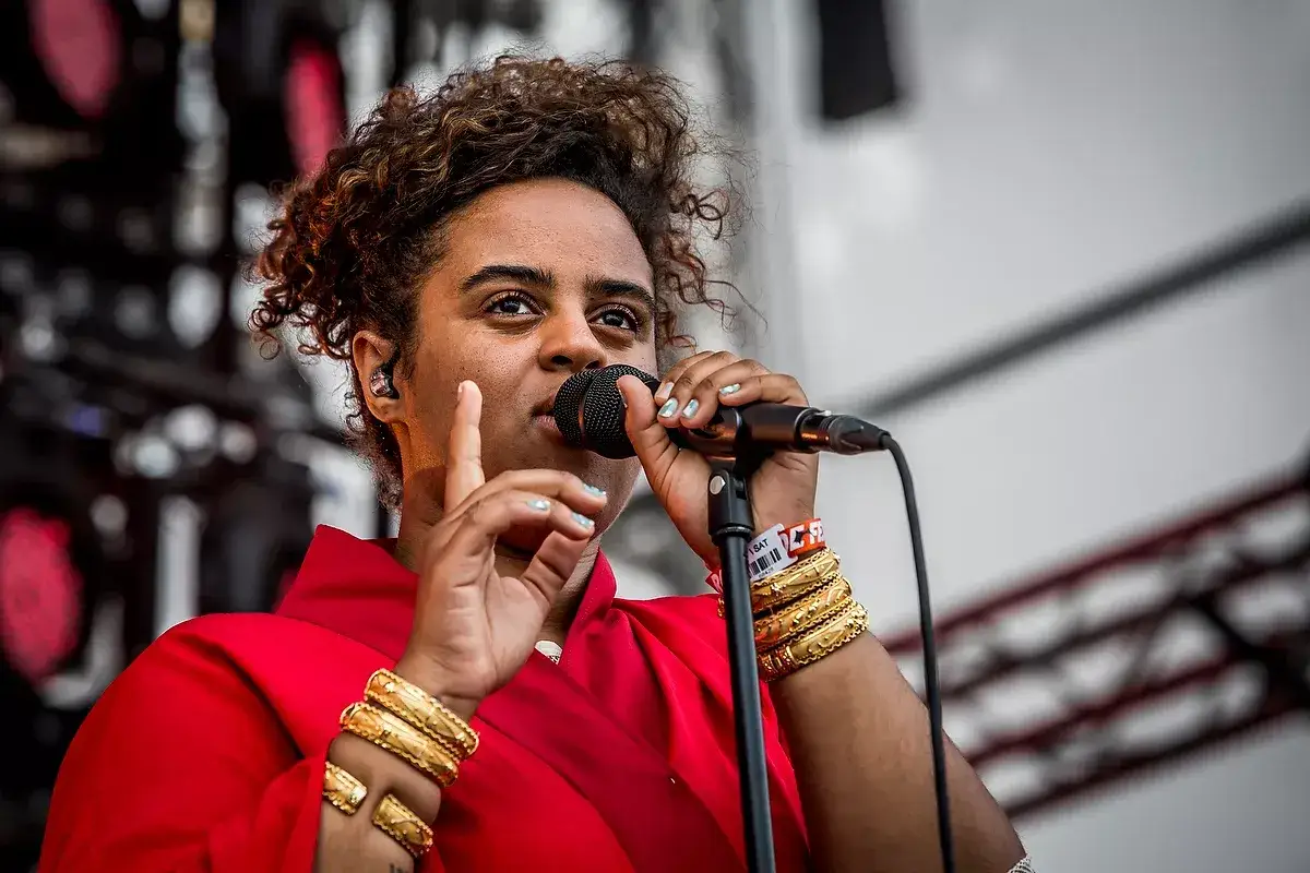 Seinabo Sey konsert. Hon sjunger i mikrofonen med en röd topp och många guldfärgade armband.
