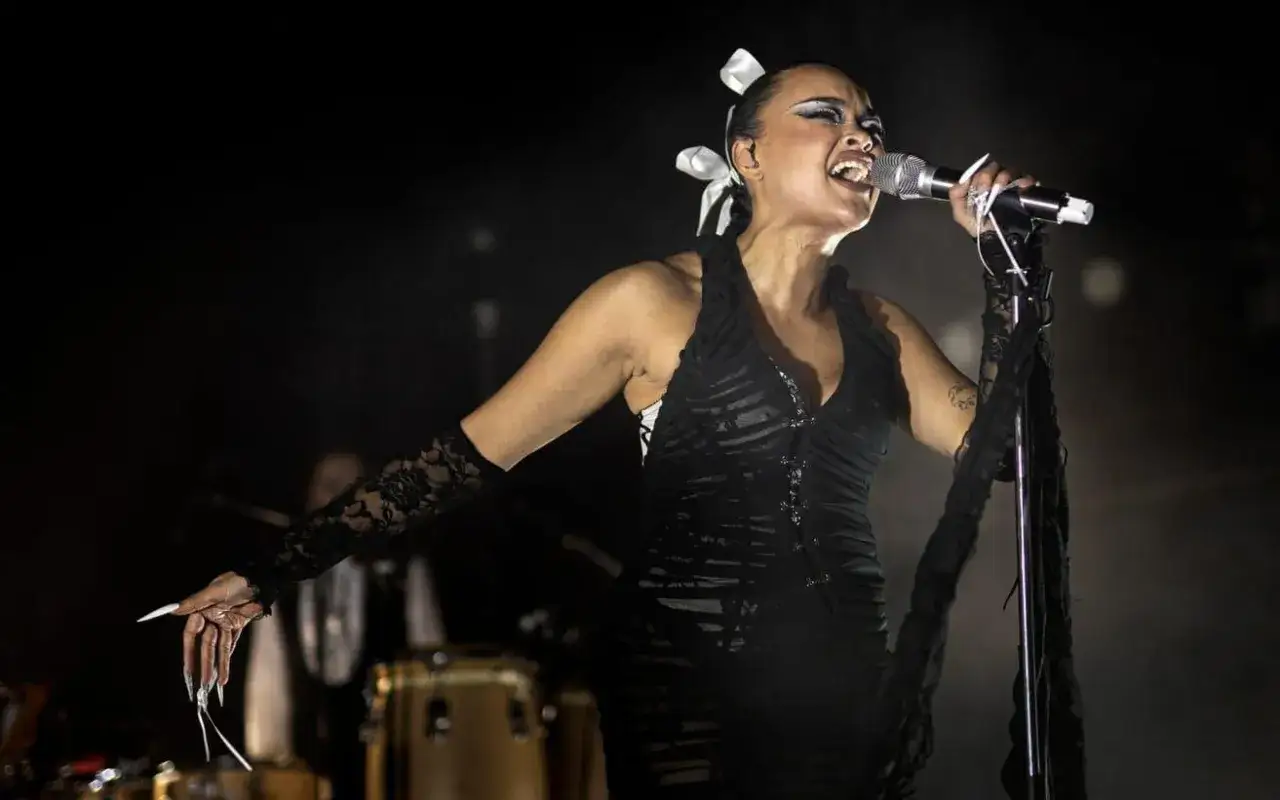 Daniela Rathana sjunger passionerat under en konsert. Hon bär en dramatisk svart klänning och spetsiga handskar.