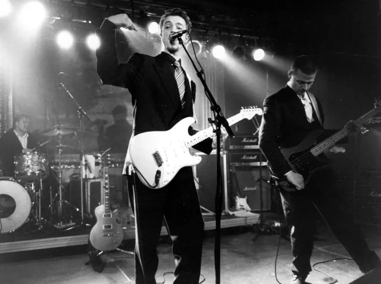 Medlemmar av The Creeps spelar live på scenen. Sångaren med vit gitarr i förgrunden, basisten till höger.