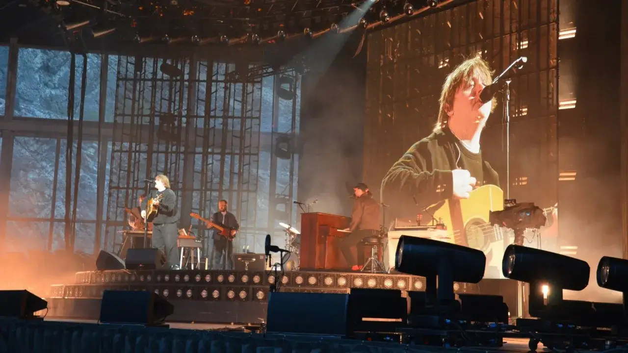 Lewis Capaldi spelar gitarr på scenen i Sverige, med en storbildsskärm bakom sig som visar en närbild av honom.