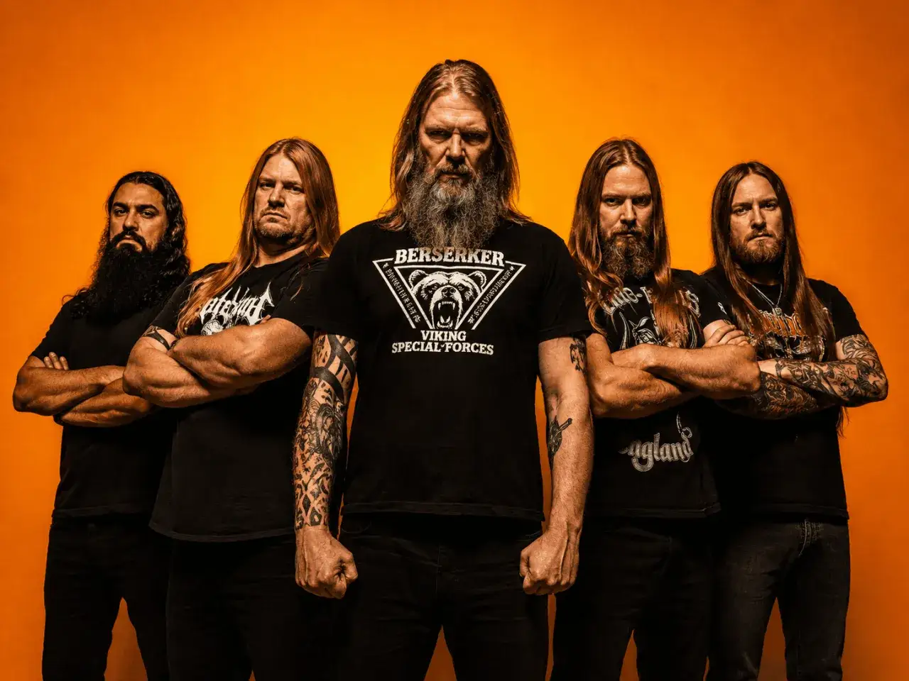 Amon Amarth tour: Fem vikingar med långt hår och skägg poserar framför orange bakgrund.