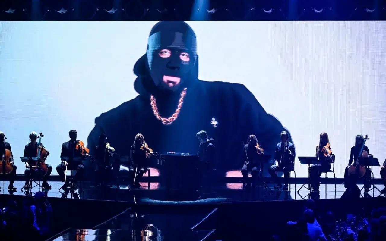 Storbild på c gambino med mask och kedja, ackompanjerad av en orkester på scen.