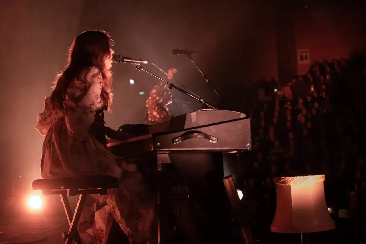 Artist spelar keyboard på scenen, publiken ser på. Kanske hon har en first aid kit pappa för att ta hand om sin röst.