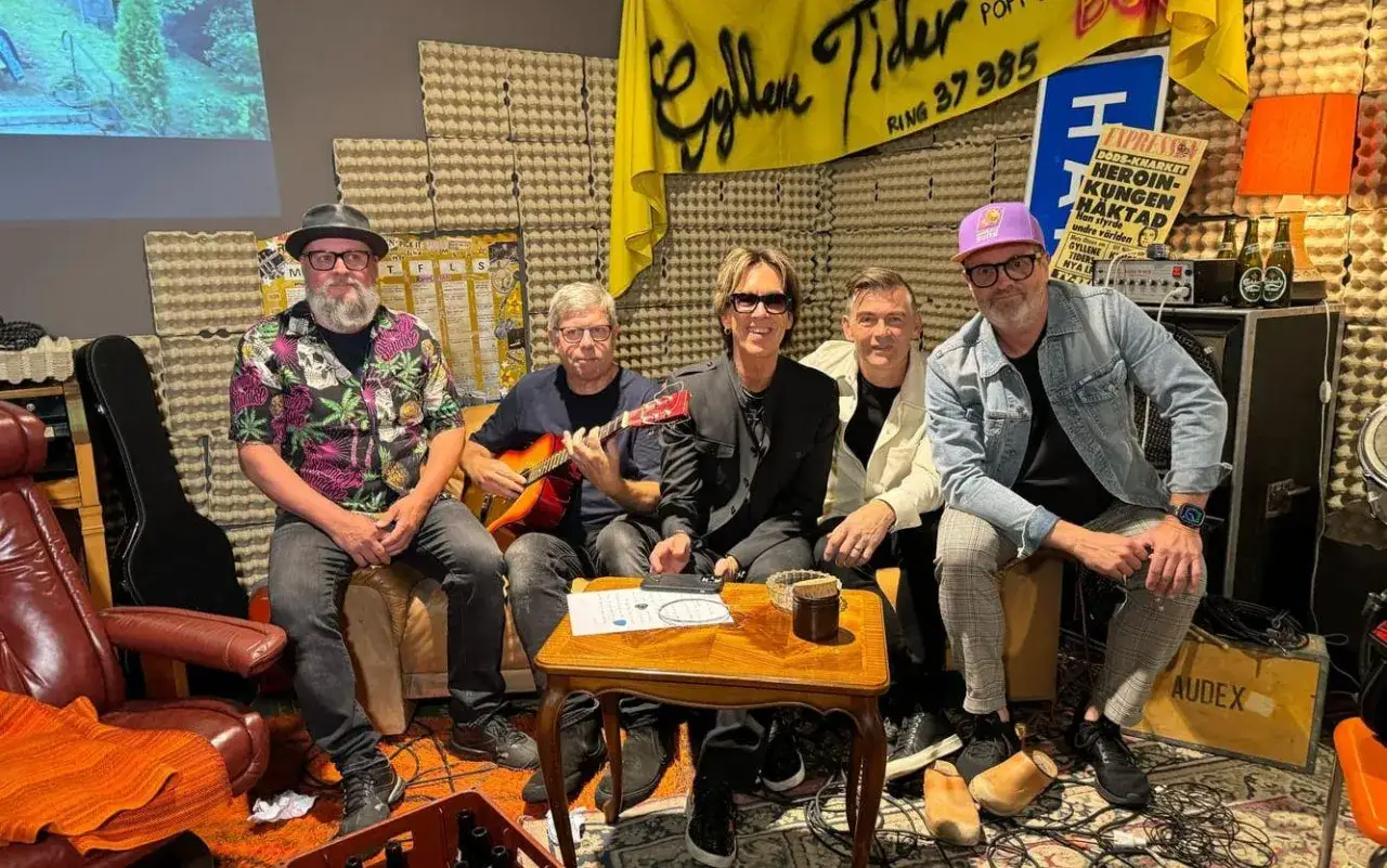 Medlemmar av Gyllene Tider samlade i en studio. En spelar gitarr, en annan bär en lila keps.
