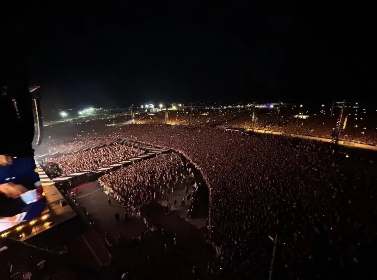 Enorm publik vid en Harry Styles konsert. Tusentals människor samlade under natthimlen, med ljus som lyser upp arenan.