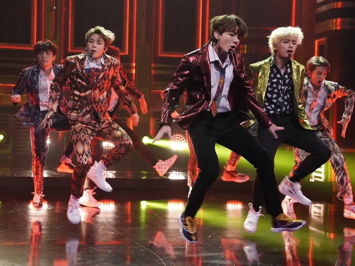 K-pop-stjärnor i glittriga kostymer dansar energiskt på scenen.