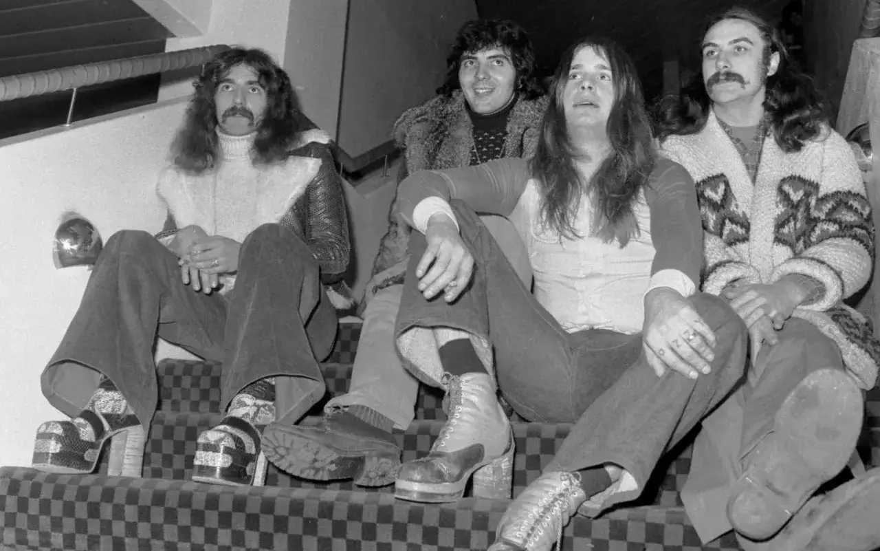 Medlemmar av Black Sabbath sitter på en rutig trappa. Tony Iommi, Geezer Butler, Ozzy Osbourne och Bill Ward.