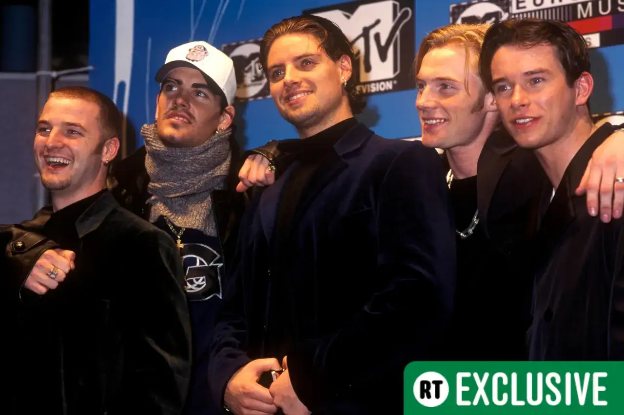 Medlemmar av Boyzone poserar glatt framför en MTV-bakgrund.