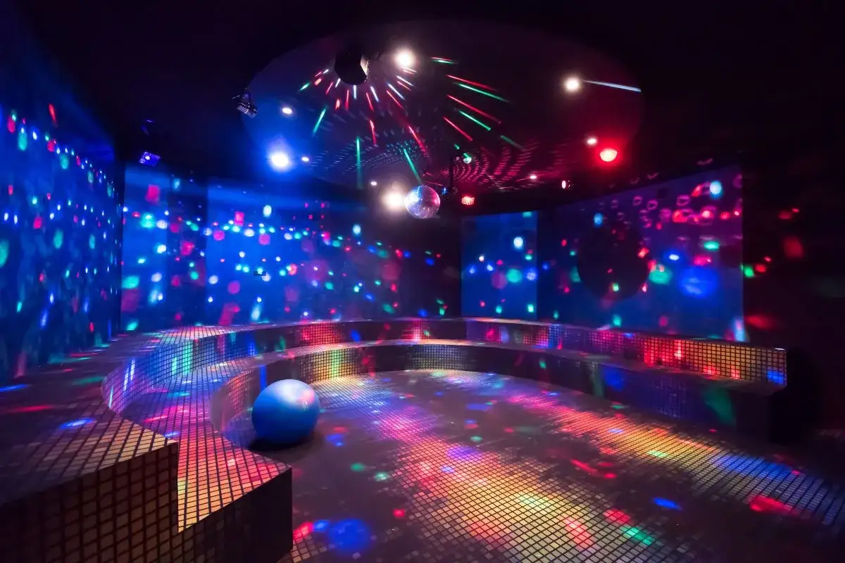 En mörk lokal med discokula och blinkande ljus i blått, rött och grönt. En blå boll ligger på golvet. Känns som en riktig 90 tals disco-fest!