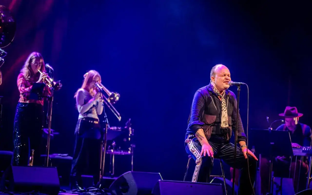 David Ritschard konsert med blåsorkester. Sångaren sitter vid mikrofonen, omgiven av musiker.