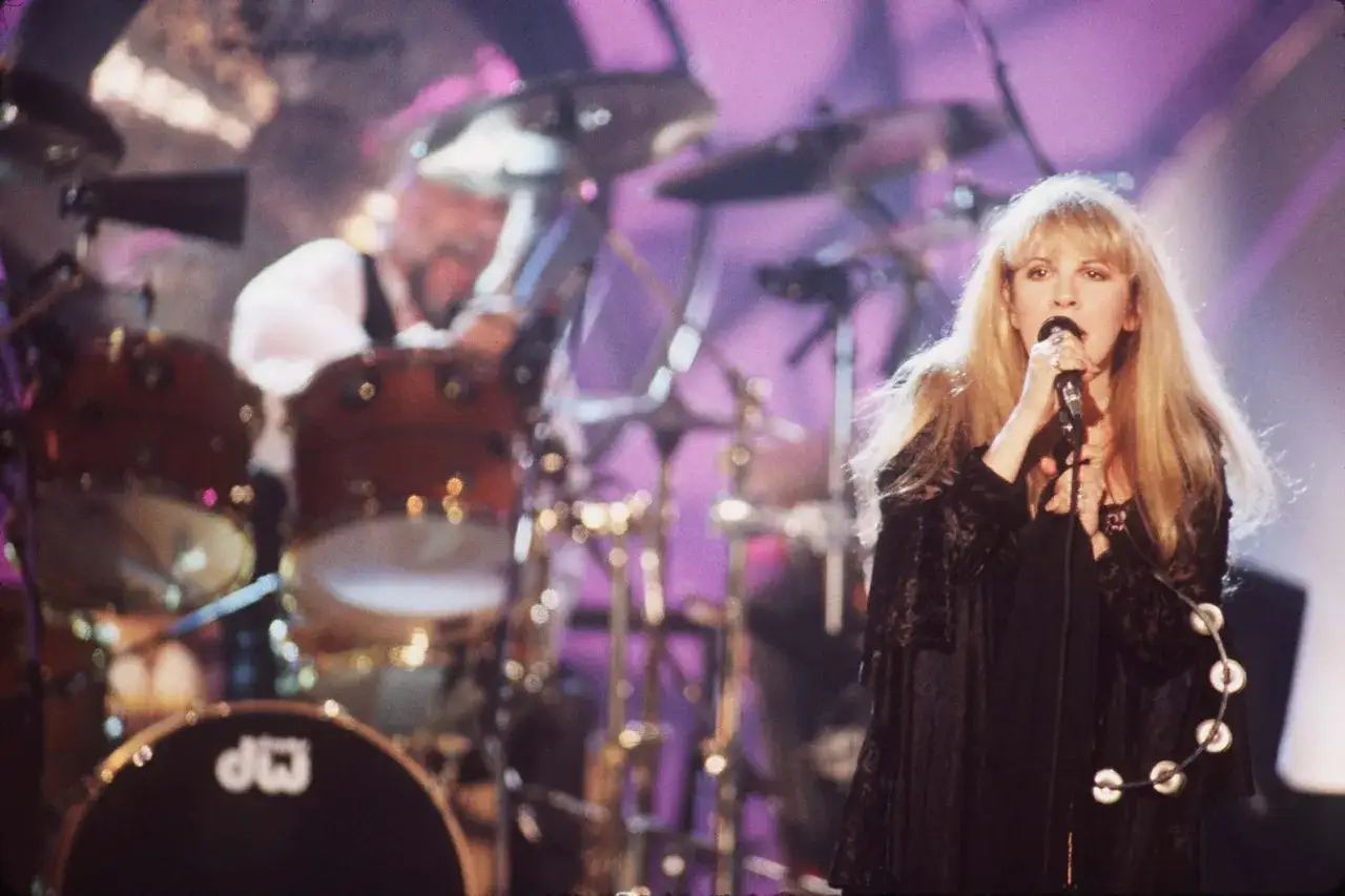 Stevie Nicks, sångerska i Fleetwood Mac, sjunger med mikrofonen i handen. I bakgrunden syns en trummis.