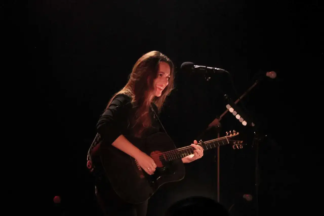 Melissa Horn spelar gitarr och ler på scenen. Missa inte kommande evenemang med Melissa Horn!