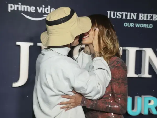 Justin Biebers fru, Hailey, ler när de kysser varandra framför en bakgrund med texten "Justin Bieber: Our World".
